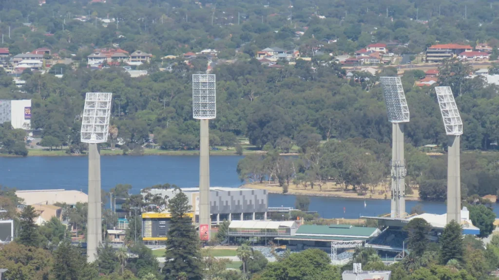 The WACA Ground in Perth seen from Central Park, with its floodlight towers, WACA scoreboard and grandstand, the Swan River behind.