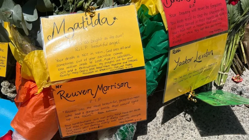 Floral tributes and handwritten memorial cards laid on the pavement at Bondi Beach.