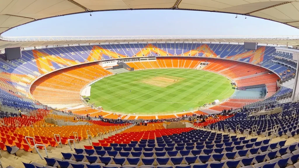 The Narendra Modi Stadium in Ahmedabad seen from the stands, showing the oval and its orange seating.