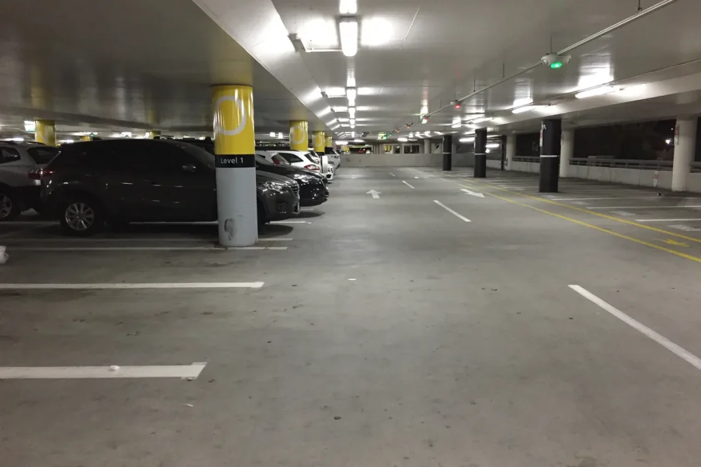 A covered level of the terminal car park at Melbourne Airport at night, lit by fluorescent lights, with a row of parked cars beside yellow and grey columns and empty marked bays.