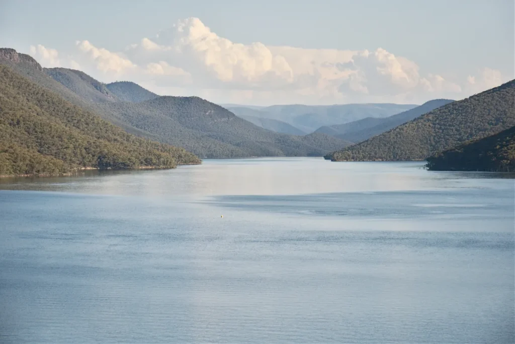 Talbingo Reservoir, a long blue lake between forested hills in the Snowy Mountains, with cumulus clouds over distant ranges